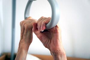 Hände einer Seniorin am Haltegriff eines Pflegebettes
