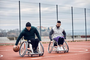 Happy men with disabilities playing wheelchair basketball on outdoor sports court.